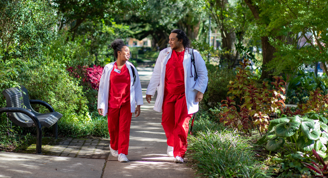 Two UL Lafayette nursing students walking underneath a canopy of oak trees on campus