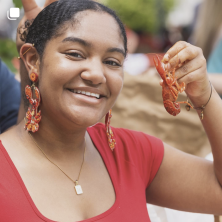 A woman wearing red and crawfish jewelry holding a crawfish